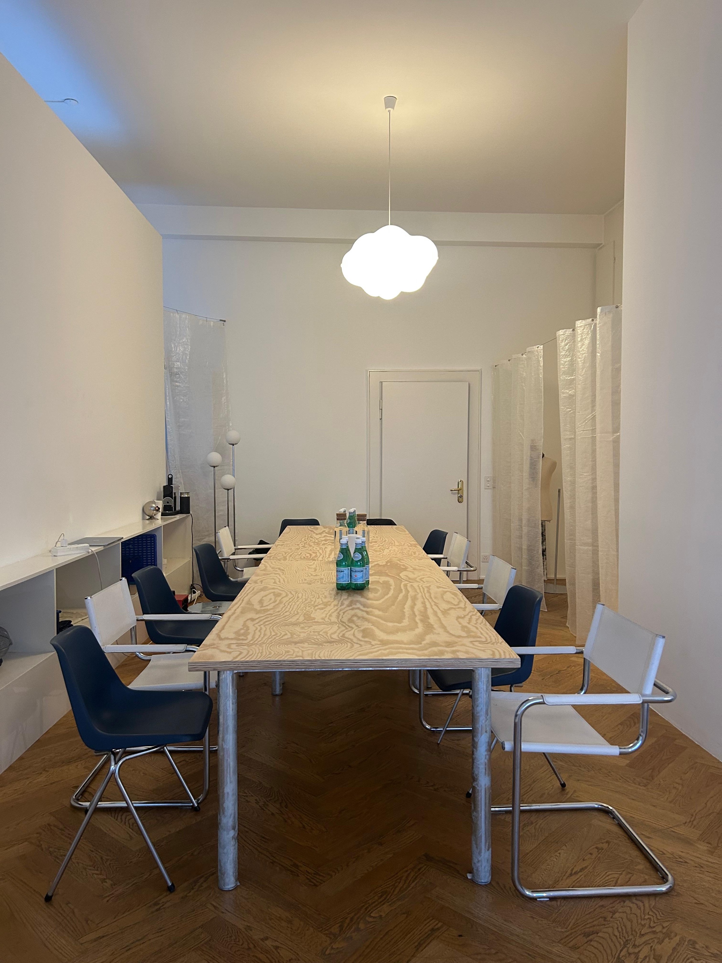 Langer Massivholztisch für Workshops, flankiert von Freischwingern, unter einer wolkenförmigen Leuchte